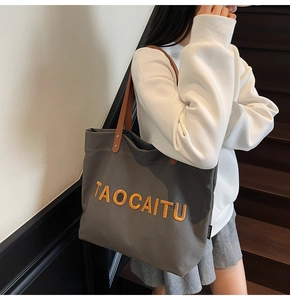 Detail of grey canvas tote bag with leather handles and orange letter branding