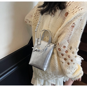 Detail of silver metallic bucket bag with knotted handle and elegant spherical charm
