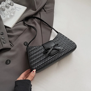 Gros plan du sac baguette tissé noir avec détail de nœud en cuir sur un bureau épuré