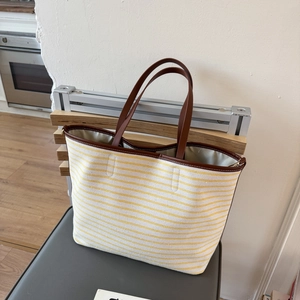 Detailed shot of yellow striped canvas tote bag with brown leather handles on wooden chair