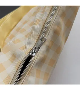 Détail de la fermeture éclair argentée et du tissu à carreaux jaune du sac