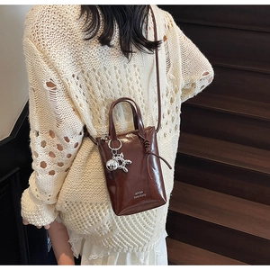 Close-up of a brown mini bucket bag with a silver balloon dog charm and white lettering