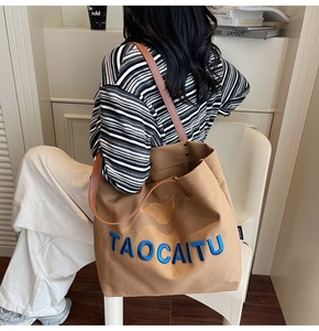 Detail of khaki canvas tote bag with blue embroidered letters and brown leather straps