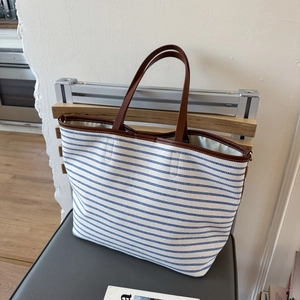 Close-up of canvas tote bag with blue stripes and premium brown leather handles