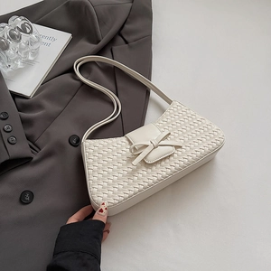 Détail du sac baguette tissé blanc crème avec nœud en cuir et longue bandoulière élégante
