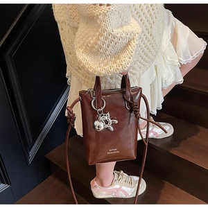 Detail of a mini brown leather bucket bag with silver hardware and a decorative charm