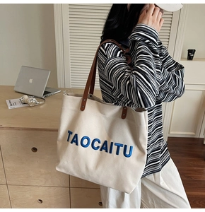 Close-up of blue TAOCAITU embroidery on a beige canvas tote bag with leather handles