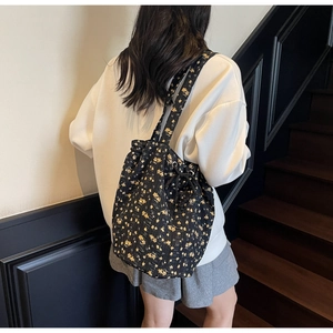 Close-up of a black floral canvas drawstring bag worn as a stylish shoulder backpack