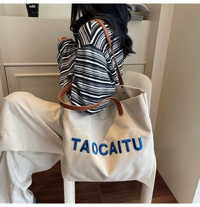 Detail of canvas tote bag showing brown leather handles and 3D blue embroidery lettering