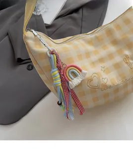 Détail du sac hobo à carreaux jaunes avec pompon arc-en-ciel sur un blazer gris