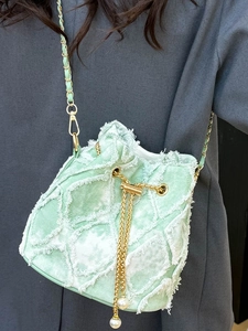 Light green denim bucket bag with frayed quilted texture and pearl drawstring accents