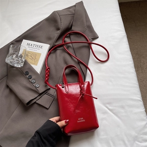 Close-up of a glossy red mini bucket bag with gold lettering and knotted strap detail