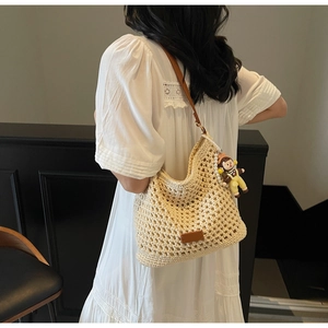 Close-up of hollow crochet shoulder bag with brown leather strap and cute doll pendant