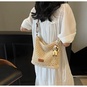 Detail of hollow-out woven crescent tote bag featuring brown leather strap and charm