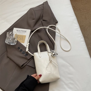 Mini white tote bag with thin strap and gold sphere charm on a stylish blazer background