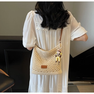 Detail of hand-woven hollow tote bag with brown leather strap and cute doll pendant