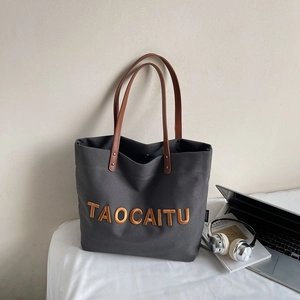 Detail of grey canvas tote bag with yellow 3D letters and brown leather handles