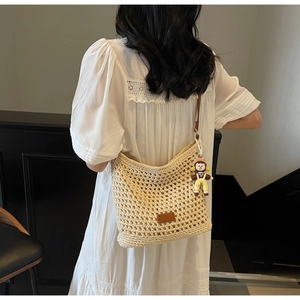 Close-up of beige woven tote bag with brown leather straps and cute doll charm