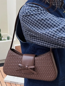 Sac hobo marron tissé avec nœud en cuir porté par un mannequin dans un cadre extérieur