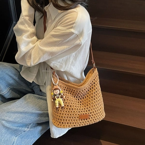 Handwoven khaki hollow tote bag with brown leather strap and decorative pendant detail