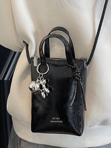Mini black glossy patent leather bucket bag with silver balloon dog charm worn crossbody