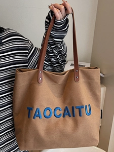 Brown canvas tote bag with blue TAOCAITU letters and leather straps in stylish daily setting