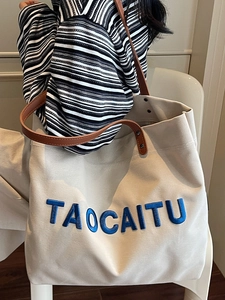 Large off-white canvas tote bag with blue embroidery and brown leather handles