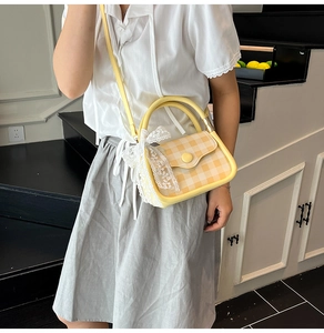 Close-up of yellow checkered mini handbag featuring a white lace bow and round decorative buckle