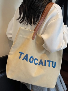 Minimalist beige canvas tote bag with brown leather handles and navy TAOCAITU embroidery