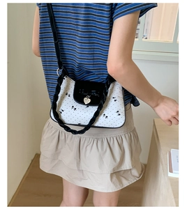 Détail d'un sac à bandoulière blanc à pois avec nœud noir et pendentif cœur doré