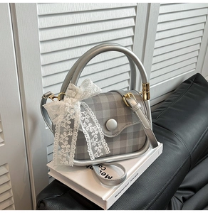 Detail view of silver handbag with grey plaid flap, round handle, and lace bow accent