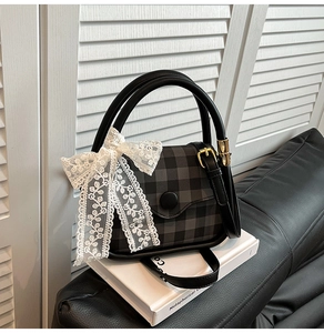 Detail of checkered square handbag featuring white lace bow and gold metal buckle
