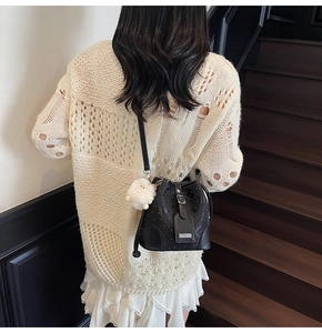 Detail of a black bucket bag with a plush lamb charm on a neutral fashion outfit