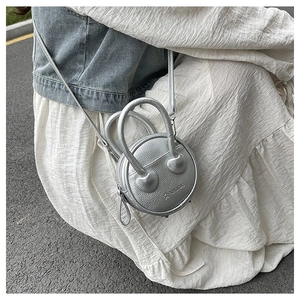 Silver round mini crossbody bag with litchi texture shown on a female model in street setting