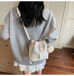 Chic cream bucket bag featuring artistic gray patterns and a plush bear charm detail