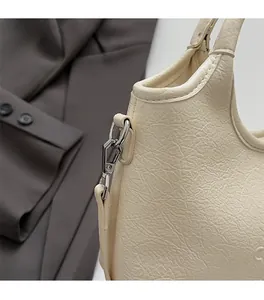 Detail von silbernem Metallhaken und D-Ring an cremefarbener Ledertasche mit Textur