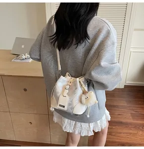 Detailed view of silver bucket bag with white leather trim and plush charm worn by model