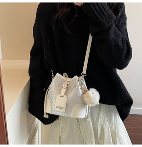 Close-up of a white bucket bag with shimmery texture and a cute plush ball pendant
