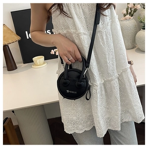 Close-up of a mini round black leather handbag with heart details on a stylish model