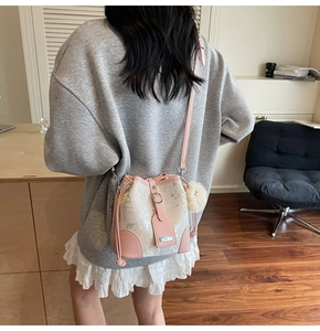 Detail view of cream white bucket bag with pink leather trim and fluffy charm on model