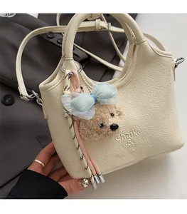 Detail einer cremefarbenen Beuteltasche aus Leder mit süßem Bären-Anhänger