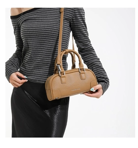 Sac baguette en cuir marron avec poignées et bandoulière porté par un modèle
