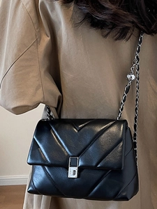 Classic black chevron quilted crossbody bag with silver buckle worn on a khaki coat