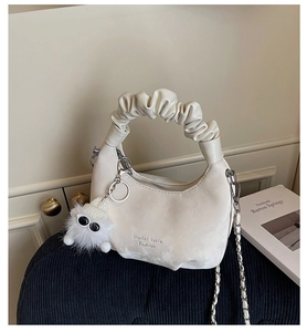Detail of creamy white crescent cloud bag with pleated handle and monster plush charm