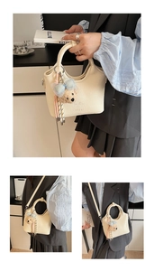 Detail der cremefarbenen Leder-Eimertasche mit Tragegriff und süßem Teddybär-Anhänger