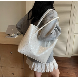Détail d'un grand sac cabas blanc à motifs chiffrés porté par un mannequin chic