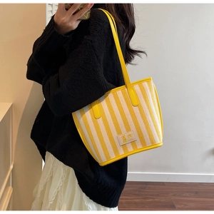 Close-up of yellow striped tote bag with 'Xi Liu' label worn by a model in casual style