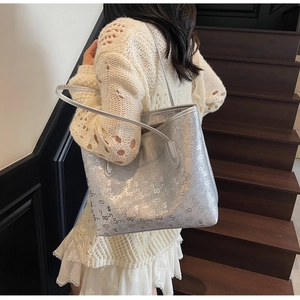 Détail du sac cabas argenté avec imprimé de lettres porté à l'épaule par le mannequin