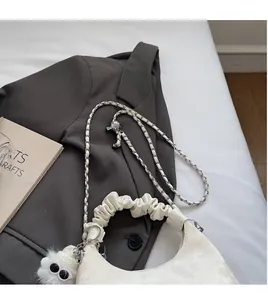 Close-up of white scrunchie handle bag with metal chain strap and plush monster charm