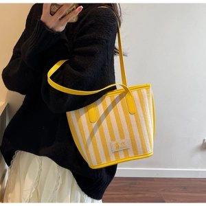 Detail of yellow striped canvas tote bag with leather handles and square logo patch